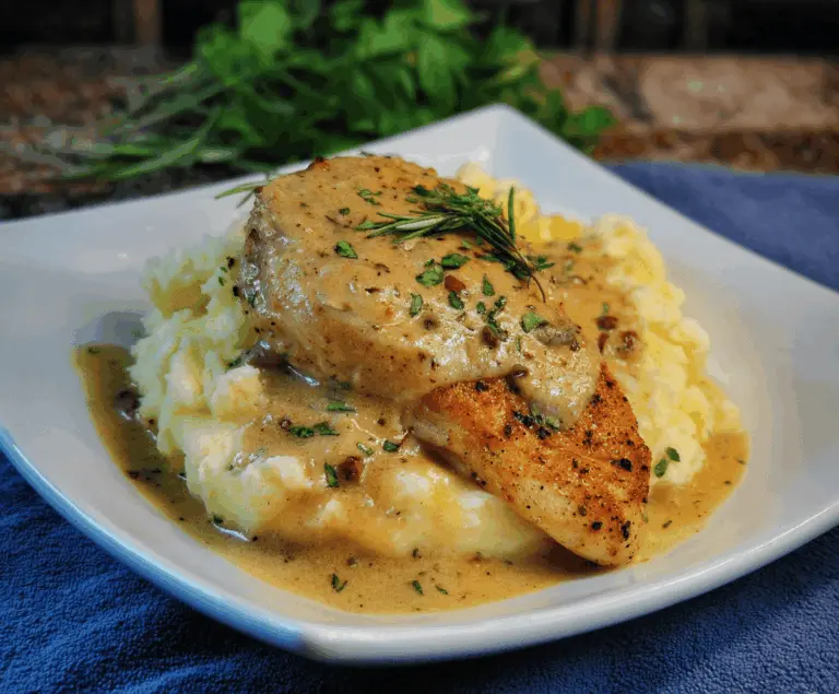 Juicy chicken topped with creamy Dijon sauce served alongside smooth mashed potatoes on a white plate.