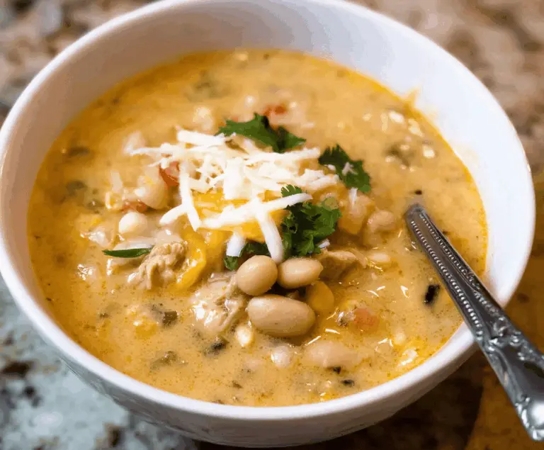 Creamy white bean enchilada soup topped with cheese and cilantro in a bowl on a rustic wooden table