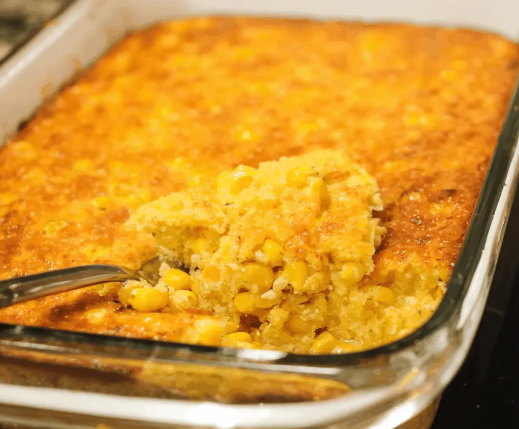 Creamy, golden corn pudding topped with melted butter and fresh herbs, served in a rustic ceramic dish, perfect for a comforting side dish