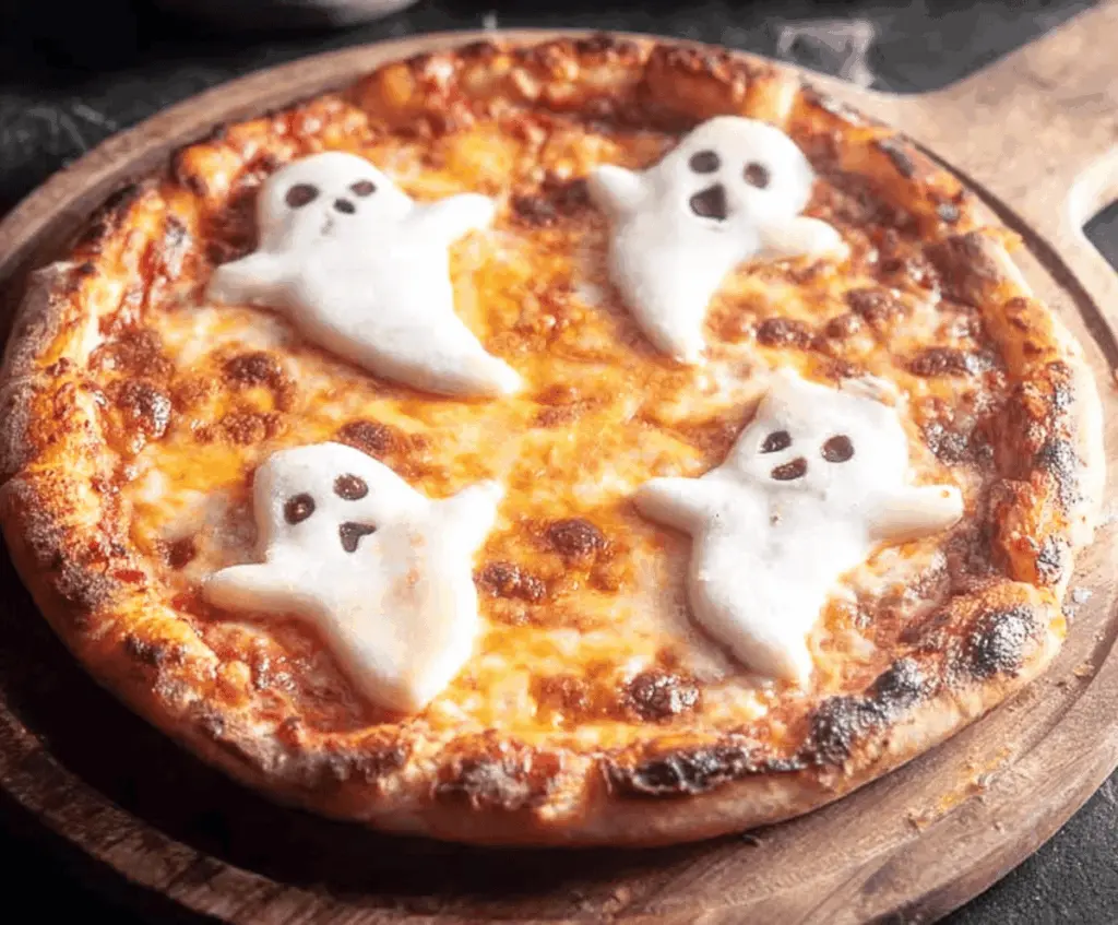 Delicious ghost-shaped pizza with mozzarella cheese and pepperoni eyes on a baking tray, perfect for Halloween-themed parties.