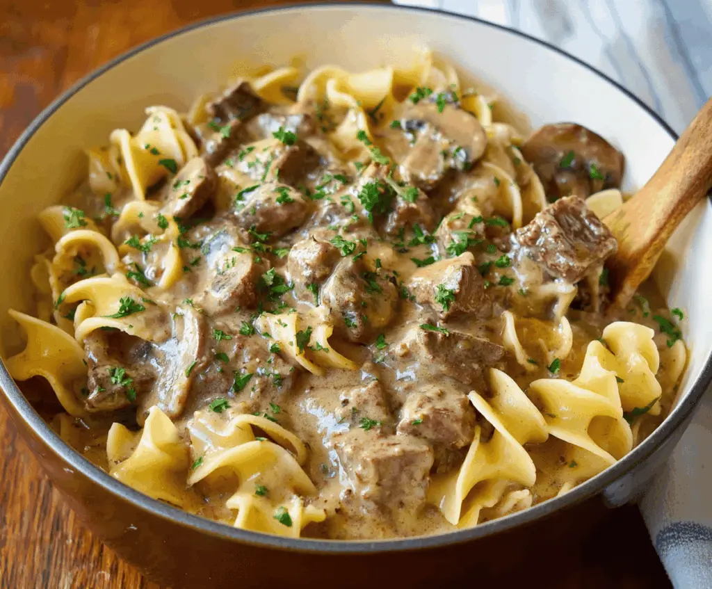 Creamy slow cooker beef stroganoff stew with tender beef chunks, mushrooms, and onions served in a rich sauce