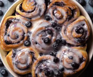 Delicious blueberry cinnamon rolls topped with icing on a white plate.