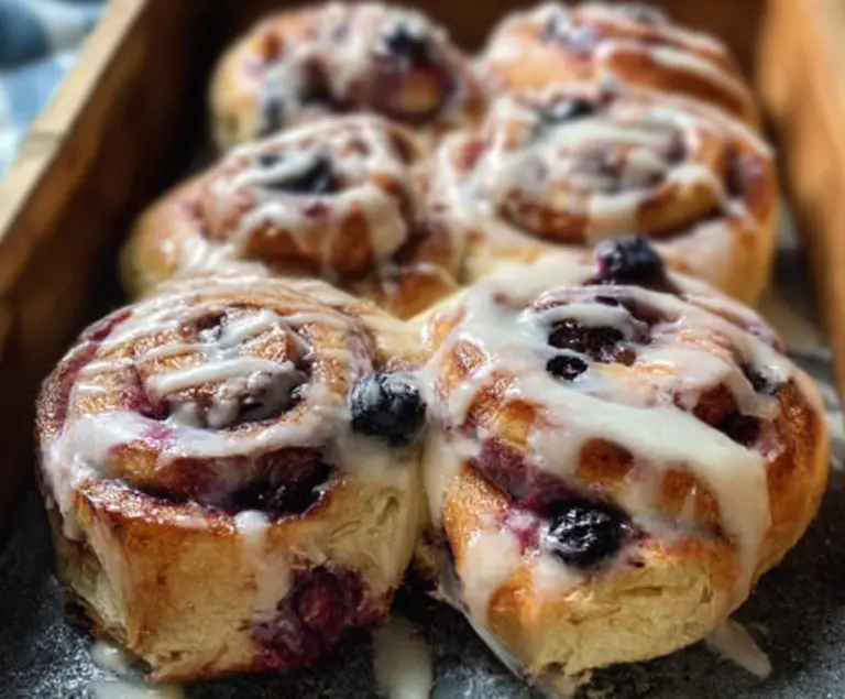 Fresh blueberry lemon sourdough sweet rolls with a golden brown crust on a wooden table.