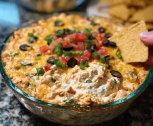 Delicious Chicken Taco Dip in a serving bowl with shredded cheese, sour cream, and chopped vegetables for a flavorful appetizer.