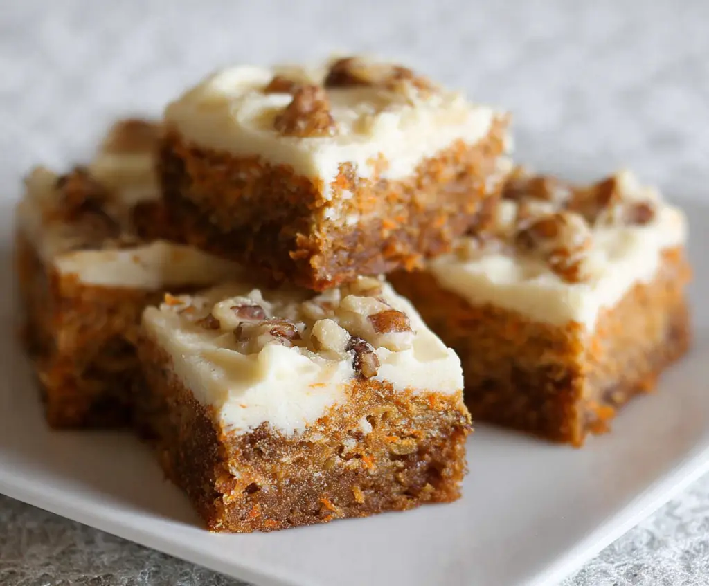 Delicious homemade carrot cake bars with cream cheese frosting on a rustic wooden surface.