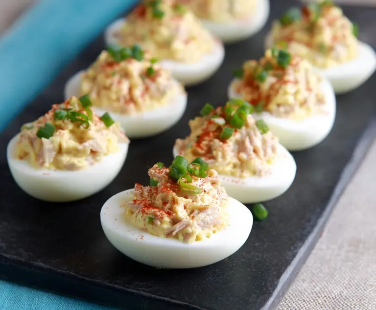 Delicious Tuna Deviled Eggs on a white plate, garnished with paprika and fresh herbs.